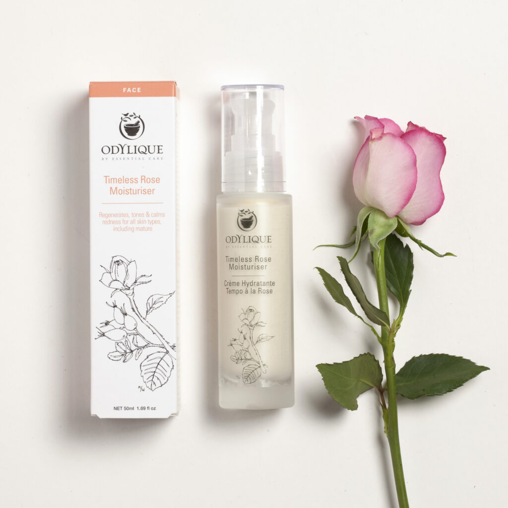 Odylique rose moisturiser bottle and box side by side next to a rose