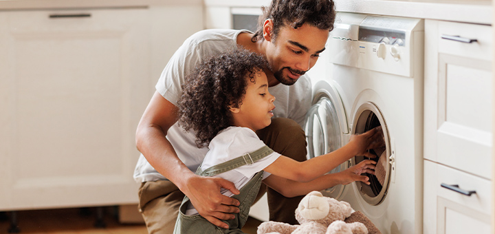 A man and a child, filling a washing machine drum.