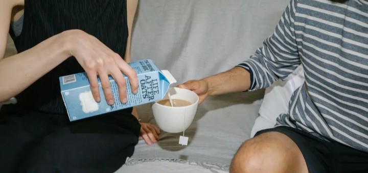 A person pouting Oatly into a cup of tea held by another person