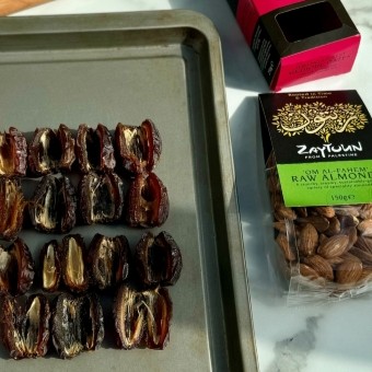 Dates lined up on a baking tray next to a packet of almonds