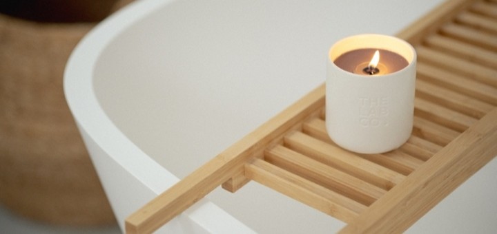 The Lab Co. energising candle lit, next to a white bath