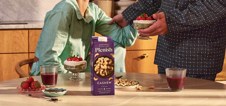 A carton of Plenish cashew milk alternative on a dining table in front of two people having breakfast.