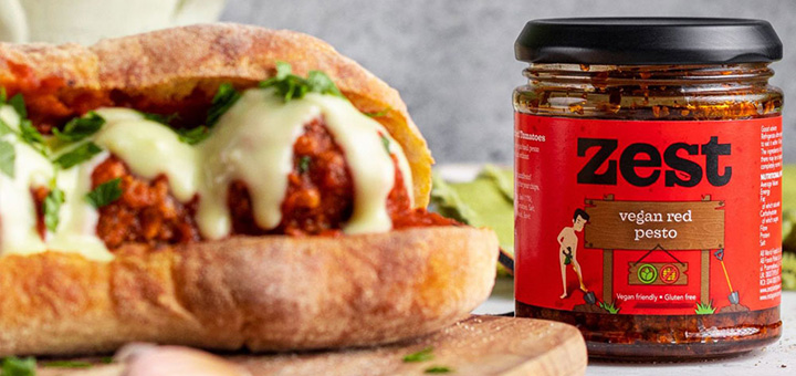 A jar of Zest vegan red pesto next to a sandwich