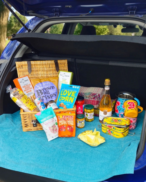 An open picnic basket filled with snacks in a car boot