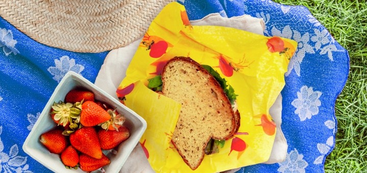 A birds eye view of a sandwich on top of a waxwrap next to some strawberries