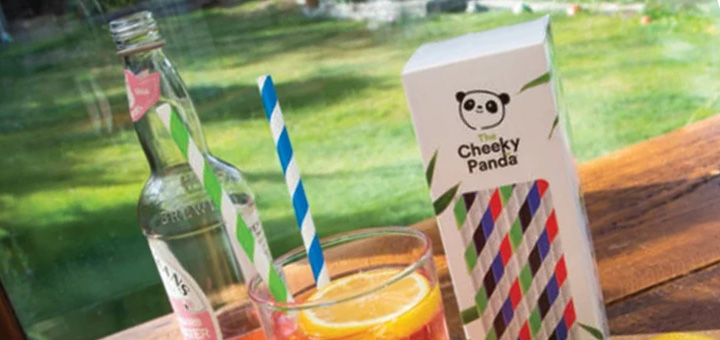A packet of The Cheeky Panda bamboo straws next to a soft drink with a straw in it on a table outside